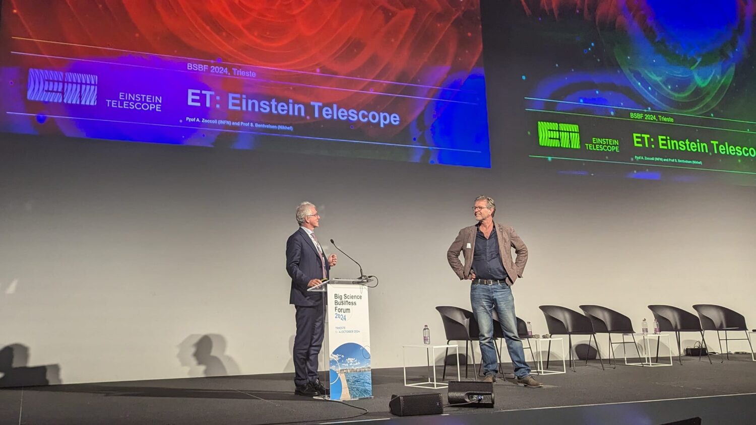 The photo shows two men presenting on stage during the BSBF meeting in Trieste 2024.